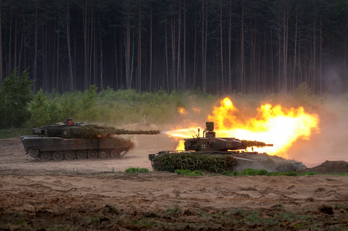 German Leopard 2 tanks firing live rounds during a combat training drill in a forested area