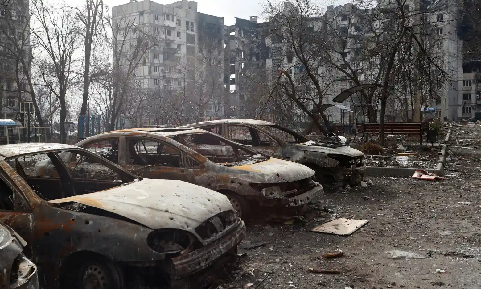 Charred cars in front of a heavily damaged apartment building in the besieged city of Mariupol, Defense Express