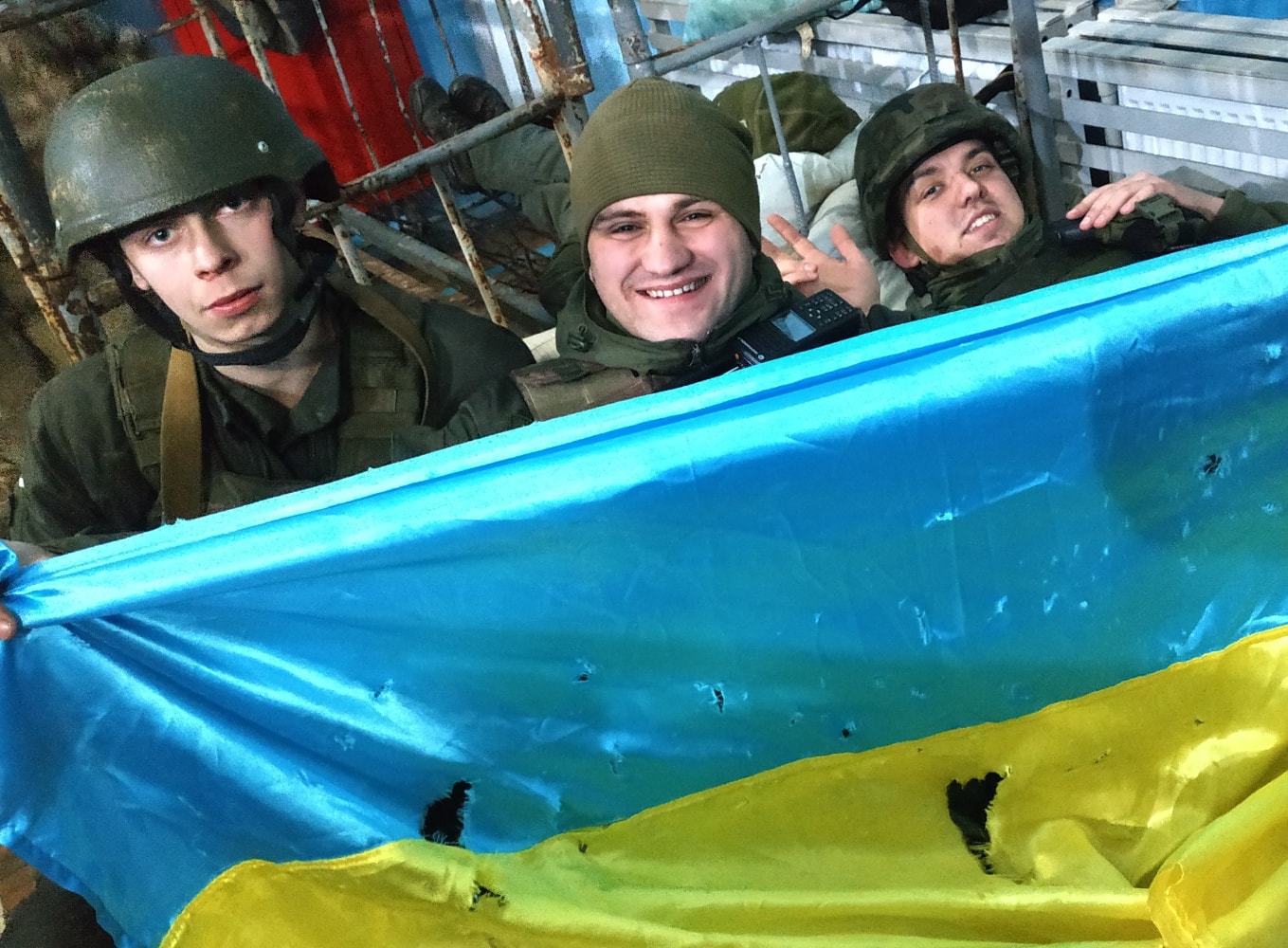 Defense Express/ Soldiers with the Ukrainian 4th Rapid Reaction Brigade pose with a Ukrainian flag after retaking the Hostomel Airport northwest of Kyiv, preventing a larger airborne assault