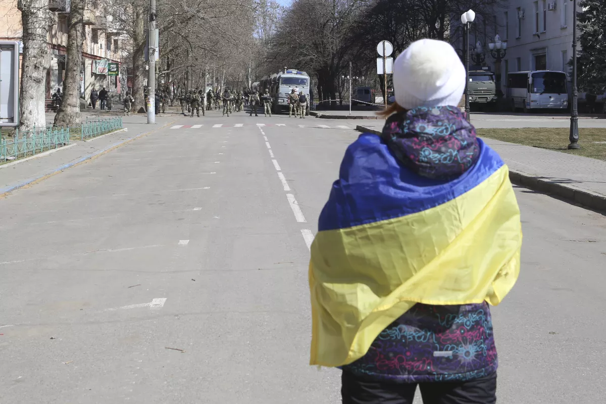 A woman wrapped in a Ukrainian flag stands in front of Russian troops during a rally against Russian occupation in Kherson, Ukraine, in March, The russian Invaders Plundering Kherson Region, Feeling That They Will Soon Have to Retreat, Defense Express