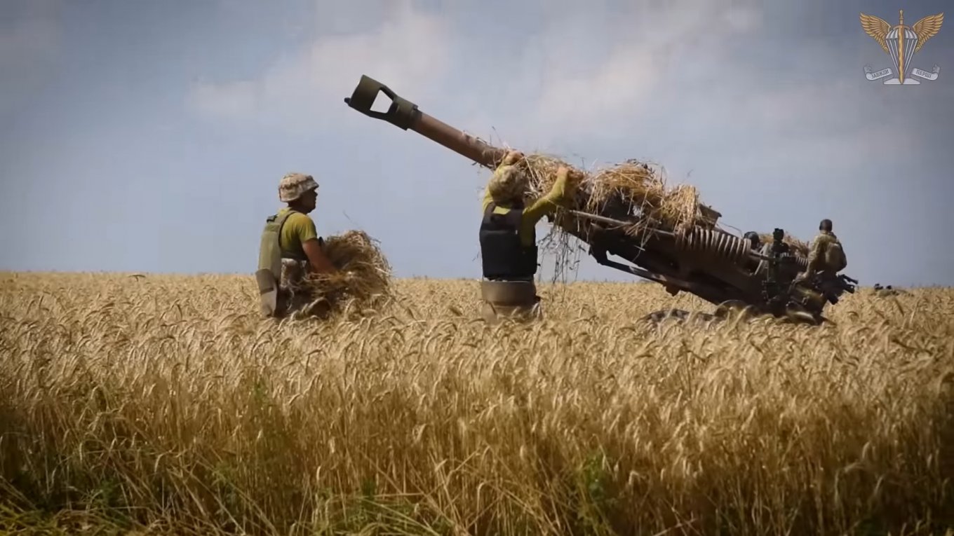 The artillerymen are covering the howitzer with greenery to camoflage it from backfire