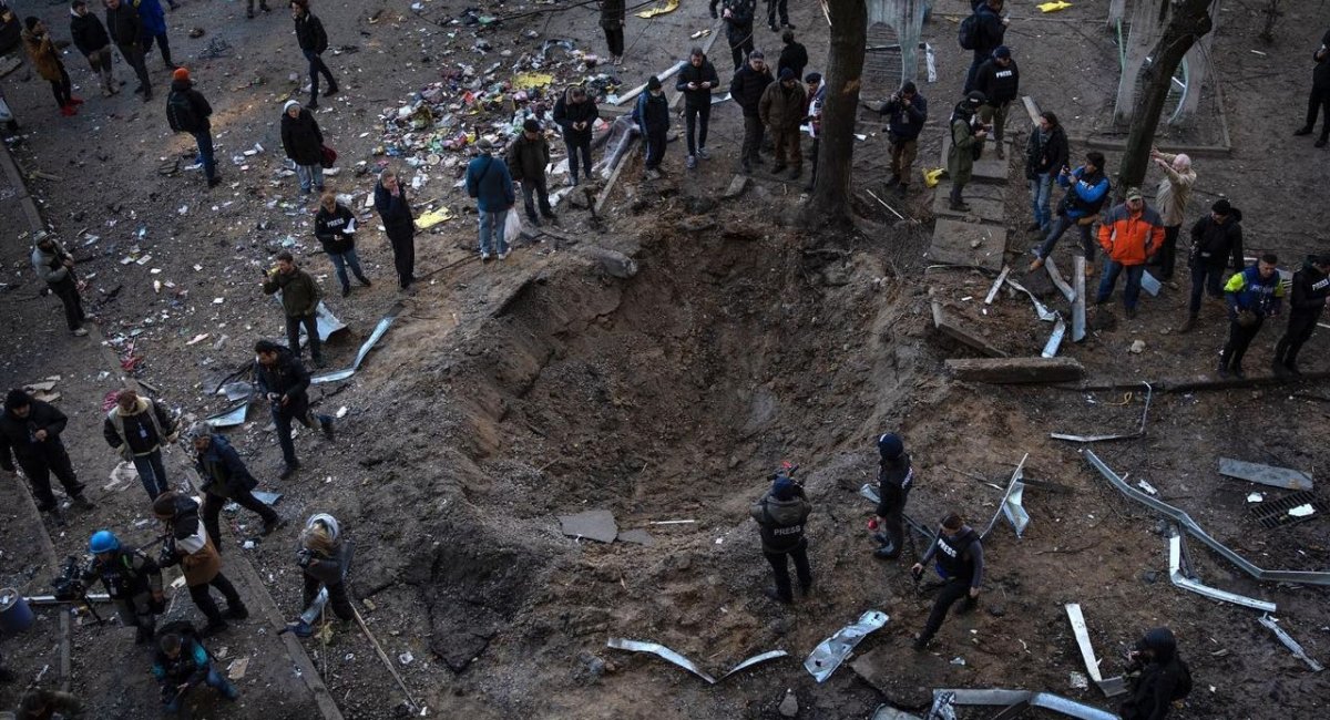People gather around a crater created by a bomb that heavily damaged buildings and cars in Kyiv, Ukraine, Sunday, March 20, 2022. / Caption & Photo credit: Associated Press, Rodrigo Abd
