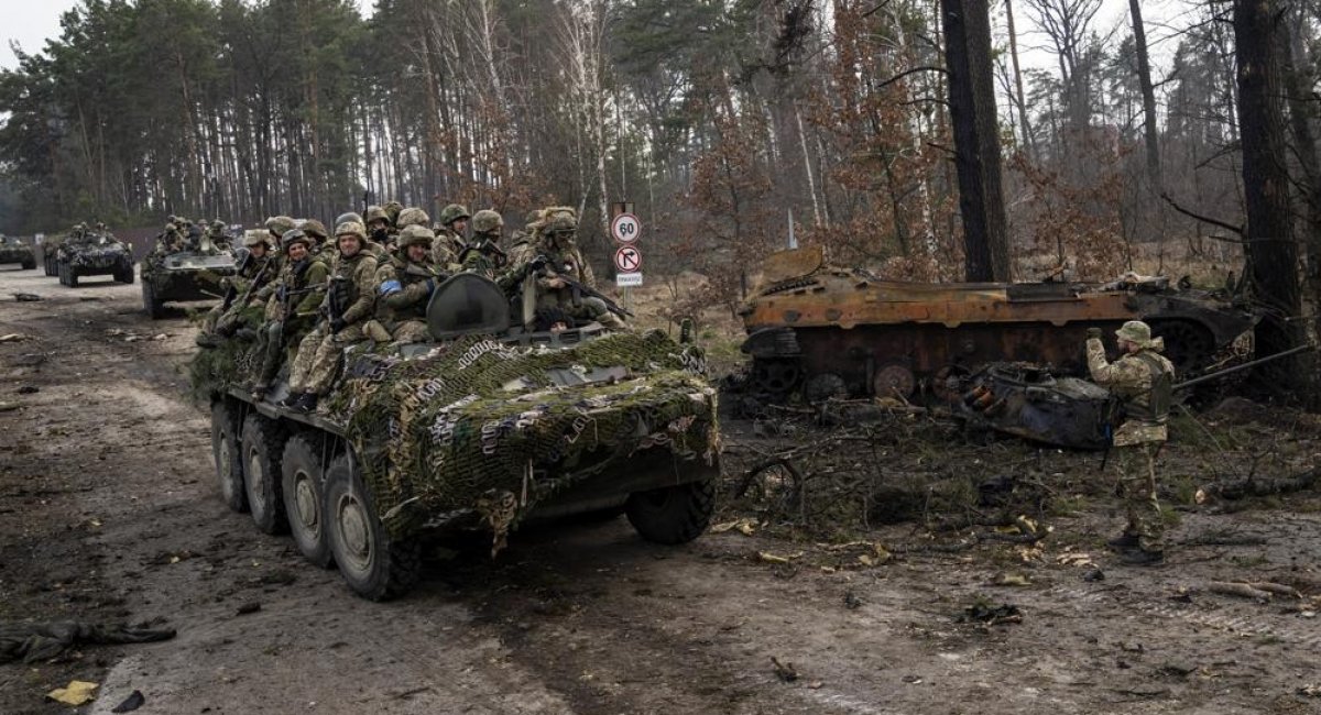 Ukrainian soldiers pass on top of armored vehicles next to a destroyed Russian tank in the outskirts of Kyiv, Ukraine, Thursday, March 31, 2022. / Caption & Photo credit: Associated Press, Rodrigo Abd